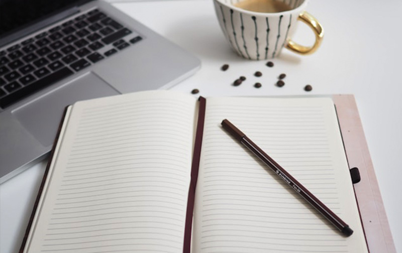 Notebook and pen on a desk next to a pc